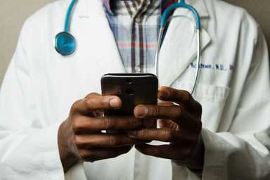 A doctor wearing a white coat and stethoscope, using a smartphone